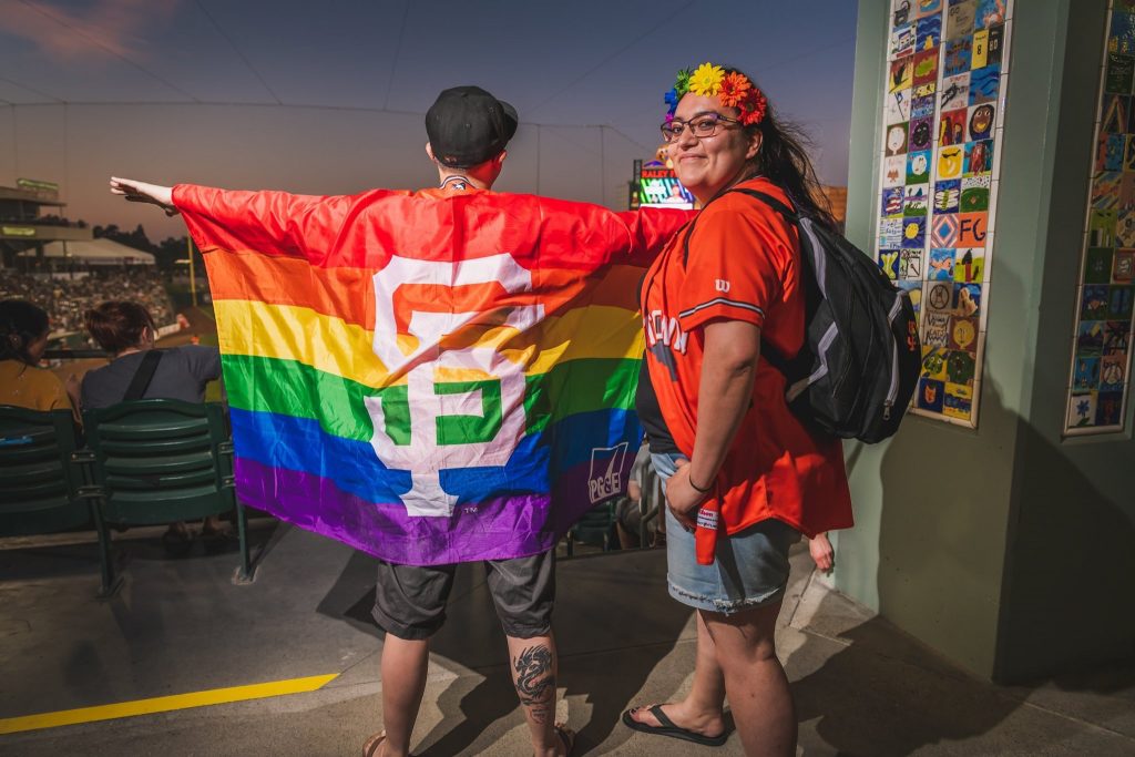 Two fans showing their pride and support with rainbow team gear at River Cats Equality Night